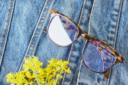 flowers and fashionable eyes glasses on a denim jacket, an old jacket from blue jeansの写真素材