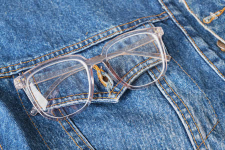 eye glasses with transparent frames on the pocket of a blue denim jacket, trend eyes glasses, retro style copy spaceの写真素材