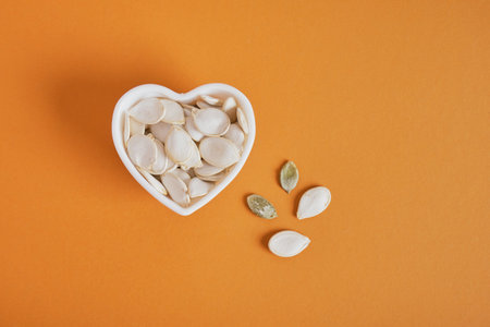 pumpkin seeds in heart shaped bowl on brown background top view copy spaceの写真素材