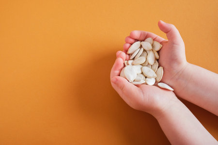 pumpkin seeds in children's palms on a brown background copy space top view