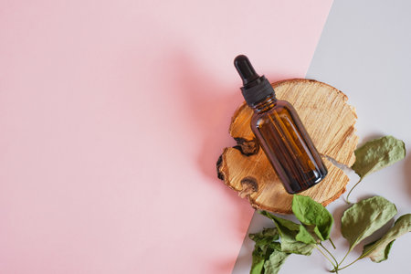 dry leaves and brown glass bottle dropper on a podium made of wood slab on a pink background, body and face skin care, serum or cosmetic oil in a bottle with a pipetteの写真素材