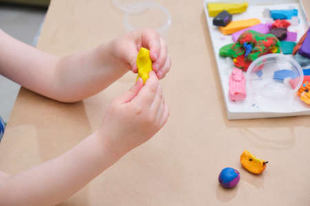 children's hands sculpt from plasticine at the table, a girl plays with plasticine copy spaceの写真素材
