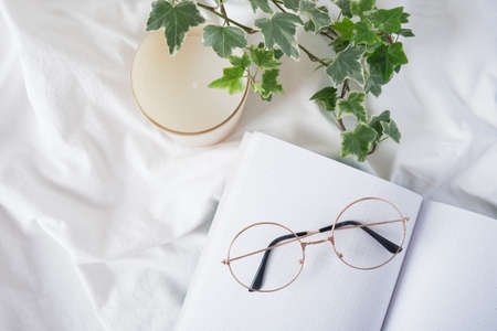 eye glasses, aroma candle, flower in a pot and open blank notepad on white crumpled cloth, planning and working at home in comfortの写真素材