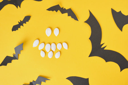 smile funny emotico from pumpkin seeds and black paper bats on yellow backgroundの写真素材
