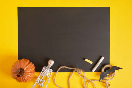 halloween mockup, blank black sheet of paper and halloween decor on a yellow background, copy space...