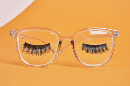 eye glasses on a concrete podium on a pink and beige background, trend composition, false eyelashes on black stylish eye glasses, copy spaceの写真素材