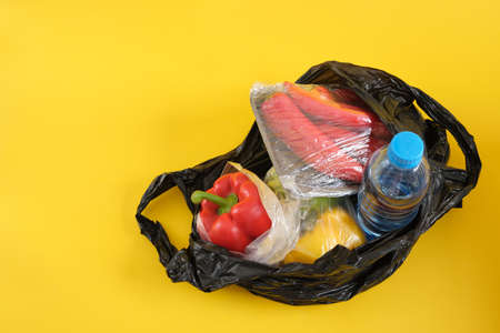 black plastic bag with groceries on yellow background copy space say no to plastic conceptの写真素材