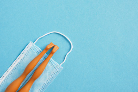 brown doll legs lie on a blue face mask on a blue background, beach vacation and tuzism during the epidemic concept copy spaceの写真素材