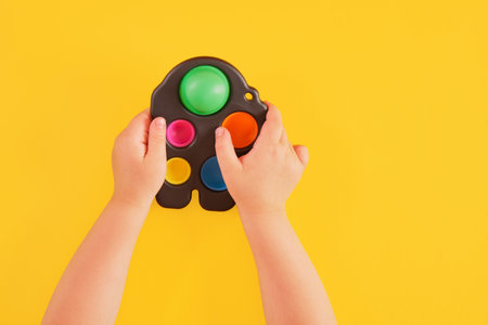colorful toy simple dimple in child's hands on a yellow background, sensory intistress toy for the development of fine motor skills of handsの写真素材