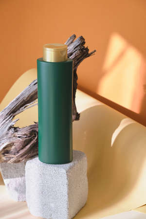 green bottle for shampoo or hair balm on a concrete podium against a background of wooden driftwood,...