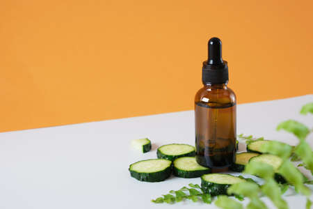 fern leaves, cucumber slices and brown glass dropper bottle on gray and brown background, natural cosmetics concept, body and face skin care, serum or cosmetic oil in a bottle with a dropperの写真素材