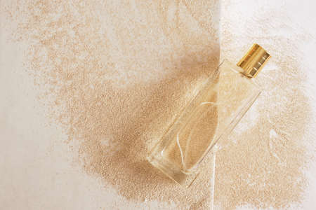transparent glass perfume bottle with golden cap withiut label on sand background copy space top...