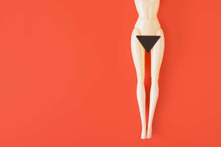 Doll and a black paper triangle on her hips red background. fenimisi art, hair removal in the bikini area copy spaceの写真素材