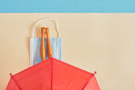 doll's legs on a protective face mask under a red umbrella on a blue and beige background, beach vacation and tourism during the   epidemic conceptの写真素材
