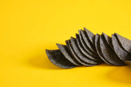 Black potato chips on yellow background. Black chips with salt, activated charcoal and red pepper.の写真素材