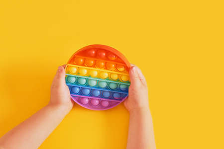 colorful toy  in child's hands on a yellow background, sensory  toy for the development of fine...