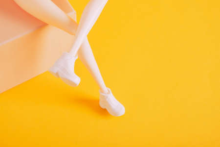 doll feet in white sneakers on a gift box yellow background copy spaceの写真素材