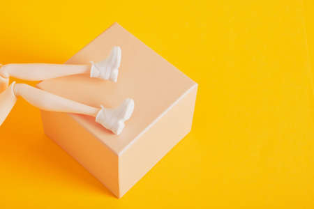 doll feet in white sneakers on a gift box yellow background copy spaceの写真素材