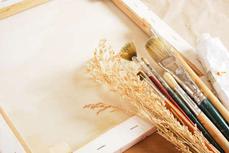 a set of brushes, paints in tubes, a wooden palette, a white canvas on a stretcher, paper and linen...