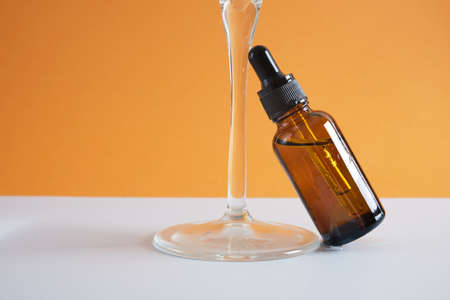 amber glass bottle with a pipette and a glass of water on a brown background, a dropper bottle for cosmetic oil or serumの写真素材