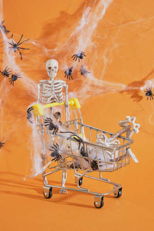 plastic decor skeleton and shopping trolley on brown background, shopping on halloween concept,...
