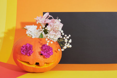 pumpkin jack lantern with flowers inside on colored background, halloween concept, day of the dead background flowers in the eyes of a pumpkinの写真素材