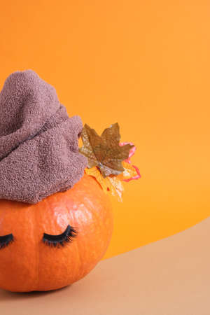 orange pumpkin with towel and false eyelashes on orange background copy space autumn skin care concept copy spaceの写真素材