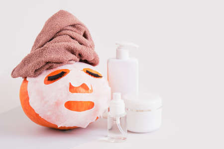 pumpkin with towel, cloth mask and false eyelashes on gray background, bottle, jar and spray with cosmetics without label mock upの写真素材
