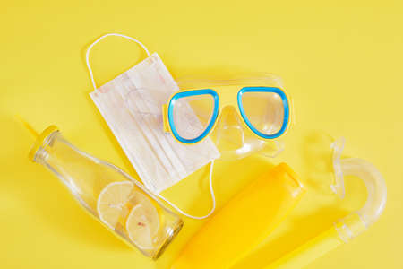 diving mask, protective medical mask, sunblock and lemonade bottle on yellow background, beach vacation concept in lockdownの写真素材