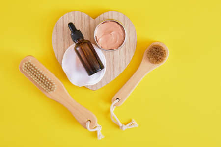face care set, cosmetic clay, wooden massage brush and amber dropper bottle, yellow background top view copy spaceの写真素材