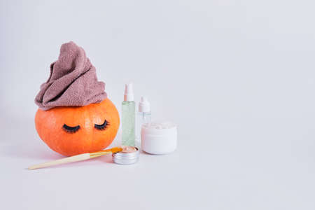 mock up set of cosmetic containers and pumpkin with towel and false eyelashes on gray background, natural skin care in autumn concept, gel, clay and bath saltの写真素材