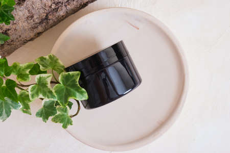 blank black jar for cosmetic cream on a ceramic podium on a beige background, tree bark and green leaves. natural cosmetics conceptの写真素材