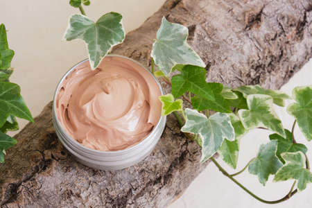 pink clay in an aluminum jar on the bark, a plant with green leaves on a light beige background...