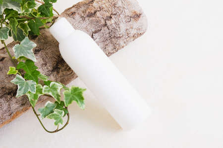 white empty bottle without label for cosmetic product, tree bark and plant with green leaves on beige background, natural body skin care, cosmetics made from natural ingredients concept copy spaceの写真素材