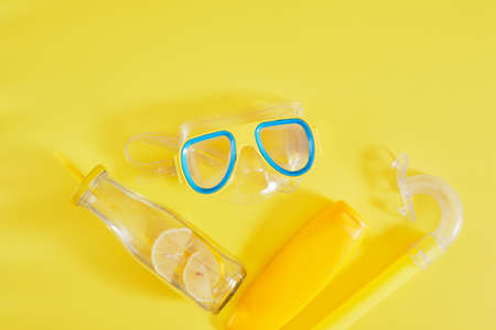 diving mask, sun cream and lemonade bottle on yellow background, beach vacation concept top viewの写真素材