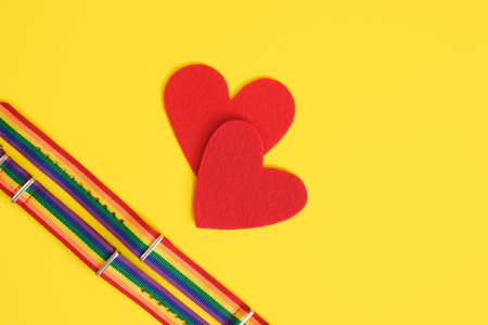 two red felt hearts and two bracelets with lgbt colors on yellow background copy space top view close up, pride conceptの写真素材