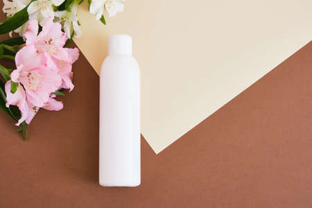lily flowers and blank mock up bottle with green cosmetics gel or lotion on beige brown background Natural cosmetic packaging. mock up beauty product concept.の写真素材