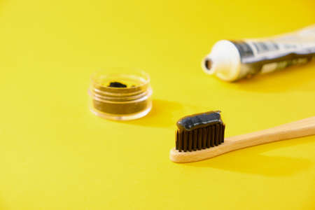 bamboo toothbrush with black charcoal toothpaste with coal yellow background tube and jar with coal charcoal black pasteの写真素材