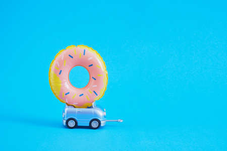 toy car and lifebuoy donut on the roof, swimming circle on the roof of a small blue golf car on a blue background copy spaceの写真素材