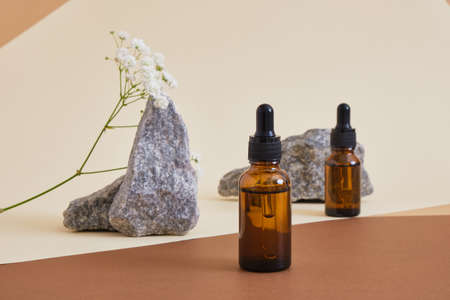 two amber glass bottles with pipette, flowers and stones on beige brown background organic cosmetic concept, serum or oil for skin careの写真素材