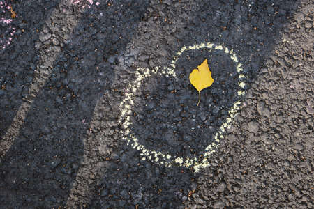 heart made with cahlk on asphalt and autumn leaf, sun light and shadowsの写真素材
