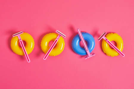 pink disposable razors on small toy balloons on pink background, body hair removal before beach...