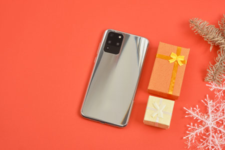smartphone with three cameras and christmas decor on red background, gifts boxes, snowflakes and phone, christmas and new year gifts conceptの写真素材