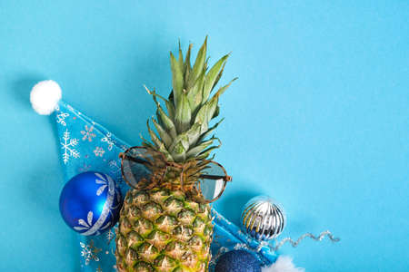pineapple in santa hat and sun glasses, christmas decor on blue background, winter vacation in tropics concept top view copy spaceの写真素材