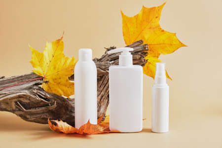 three different white mock-up bottles without a label for cosmetics on a background of driftwood and autumn leaves, beige background, natural cosmetics concept, autumn skin careの写真素材