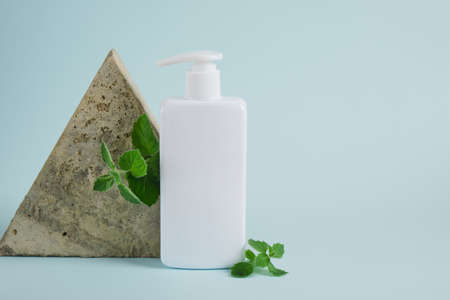 cosmetic bottle with dispenser and fresh mint on light blue background. Organic cosmetics concept. Cosmetic container mockup without label Natural skincare product.の写真素材