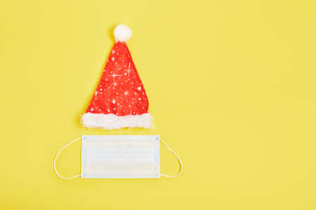 Red Santa hat and medical mask on yellow background, copy space, top view mock upの写真素材