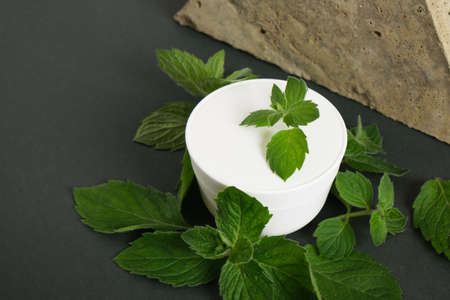 stone, cosmetic white cream jar and fresh mint on dark green background. Organic cosmetics concept. Cosmetic container mockup without label Natural skincare product.の写真素材