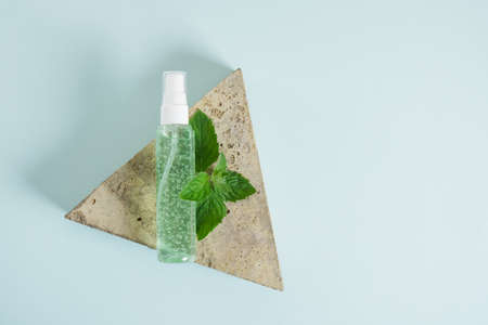 triangular stone, cosmetic bottle with green gel and fresh mint on triangular stone light blue background. Eco Natural cosmetic product concept. Organic skin care product with peppermint oilの写真素材