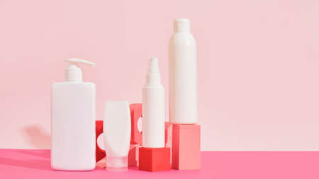 several different white plastic bottles and tube on pink geometric podiums on pink background Cosmetic mock up bottles. Branding identity mockup concept.の写真素材